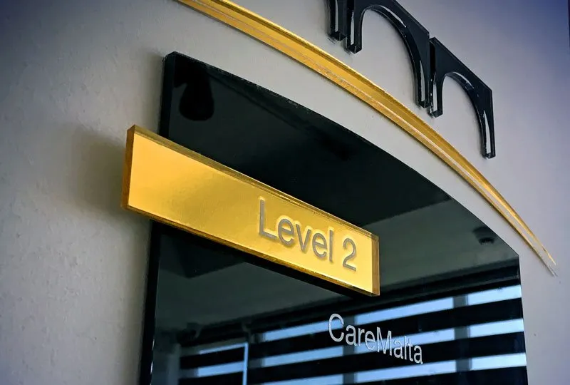 A gold Level 2 floor sign mounted on black glass in a CareMalta building