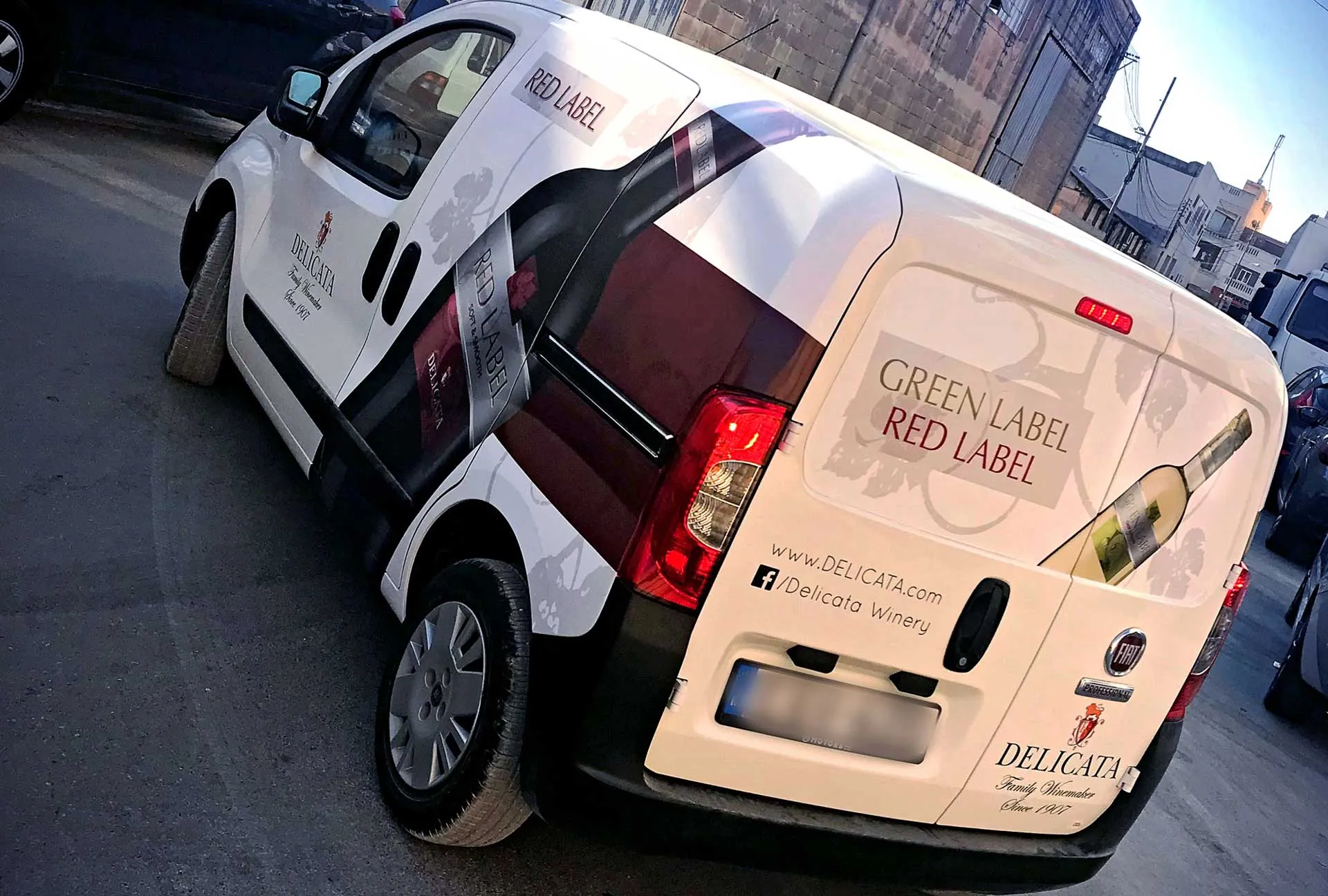 A white Delicata van wrapped for the Green Label and Red Label range, seen from the rear