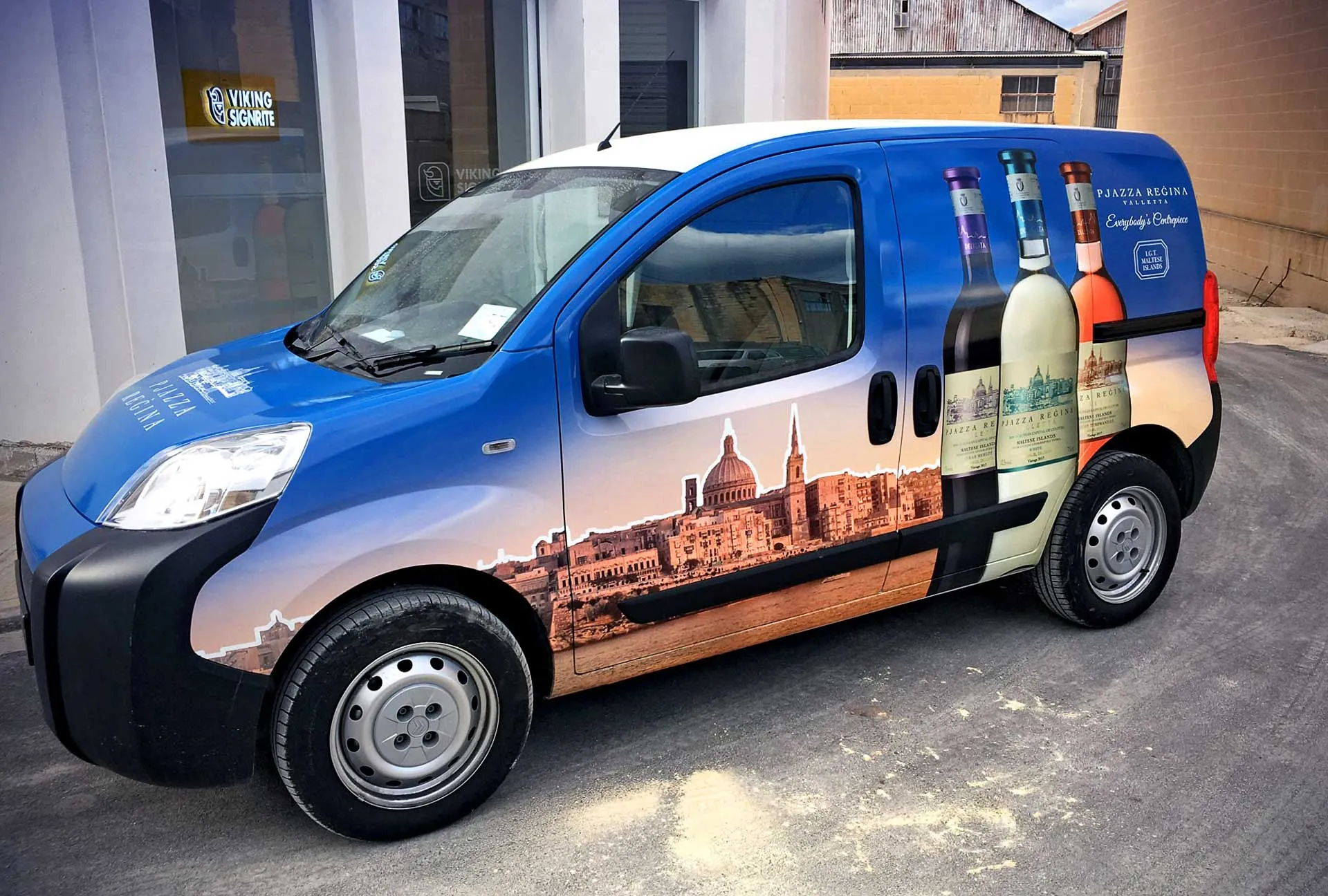 A blue Delicata van wrapped with the Pjazza Reġina wine range and a Valletta skyline along its flank