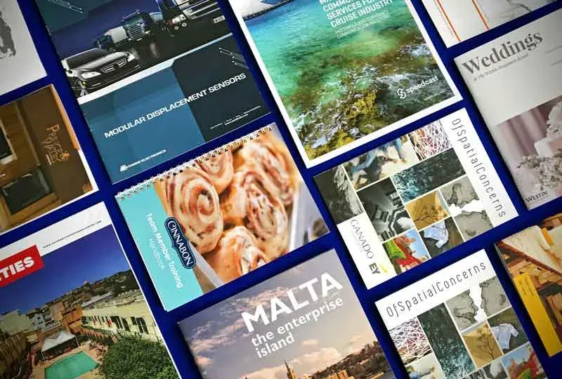 Printed booklets, brochures and magazine covers fanned out across a blue surface